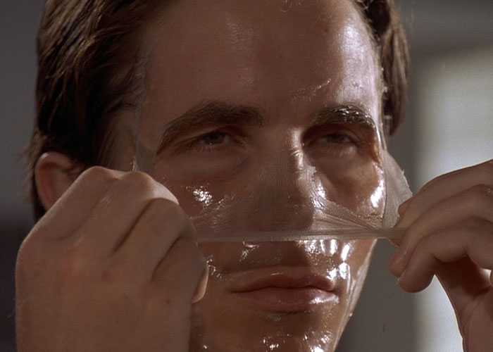 Close-up of a man peeling off a translucent mask, a scene from a surprising film adaptation that outdid its book.