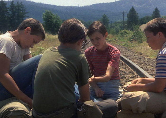 Four boys sitting by railroad tracks in a classic film scene representing surprising film adaptations that outdid their books.