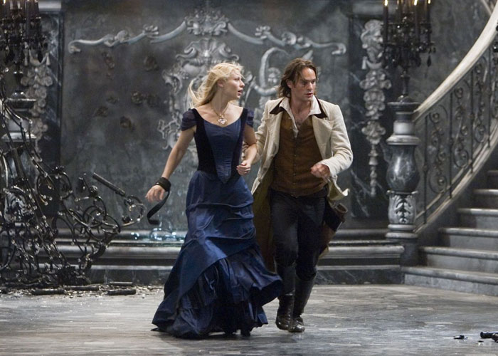 Scene from a surprising film adaptation showing a man and woman in period costumes running inside an ornate mansion.