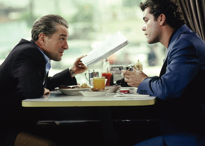 Two men having an intense conversation over breakfast, illustrating a scene from surprising film adaptations outdoing their books.