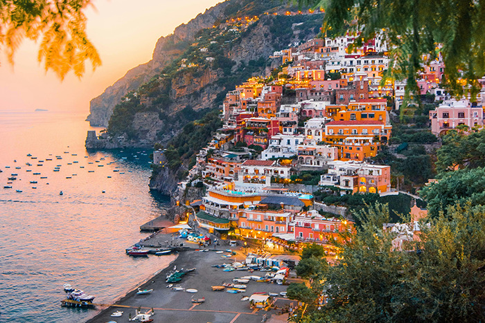 Coastal cliffside village at sunset with colorful houses and boats, a popular place visited and loved by travelers
