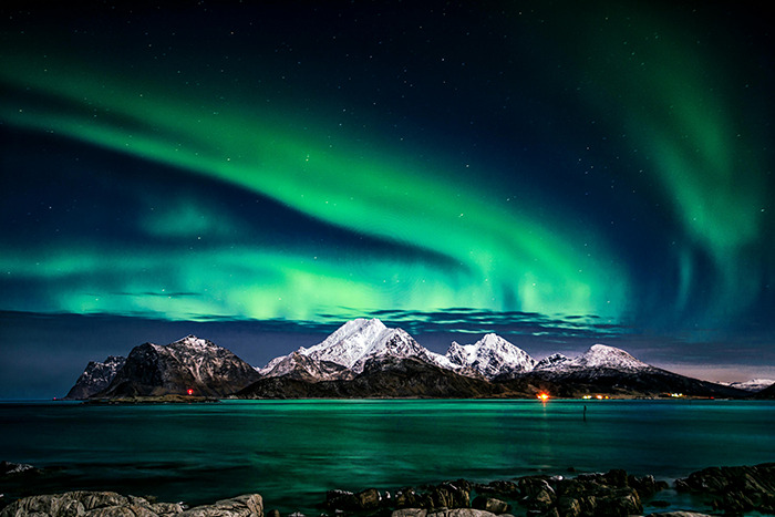 Aurora borealis over snowy island mountains and sea, breathtaking place visited that exceeded the hype