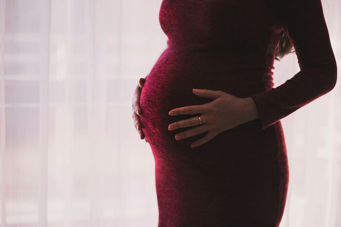 Pregnant woman in a red dress gently holding her belly, highlighting emotional moments during pregnancy.