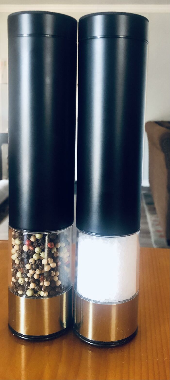 Black and brass salt and pepper grinders filled with peppercorns and salt crystals on a wooden surface