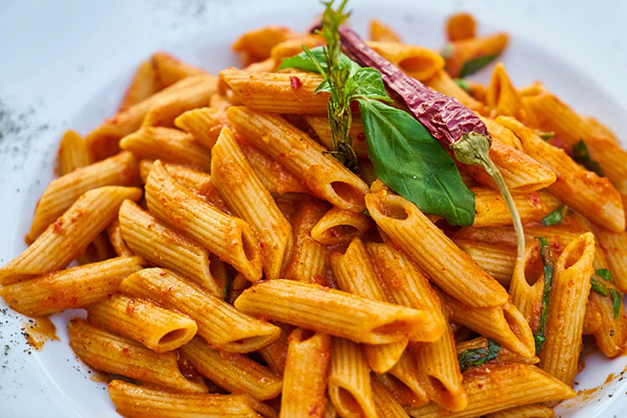 Close-up of spicy penne pasta garnished with basil and a dried chili, illustrating stereotypes about home countries food.