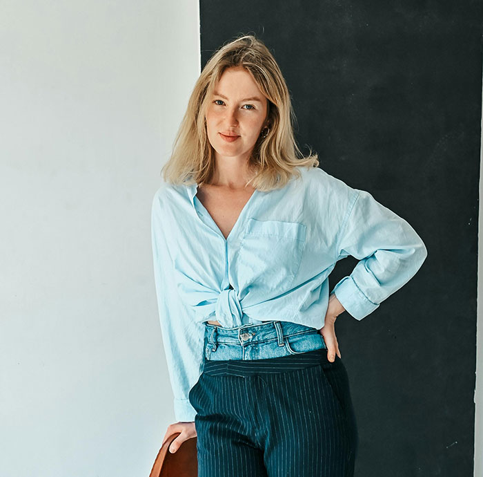 Young woman in casual shirt and striped pants posing indoors, illustrating hilarious stereotypes about home countries.