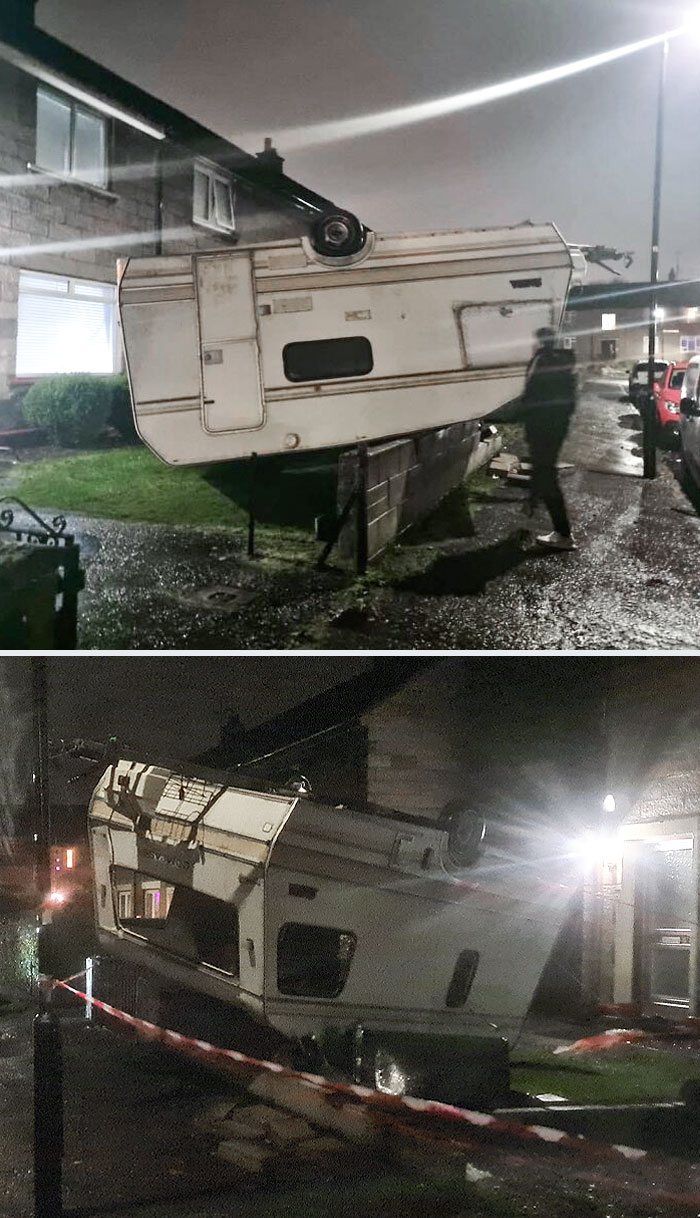 Upside-down camper trailer precariously balanced on a house roof, showcasing wild nature's unexpected forces at night.