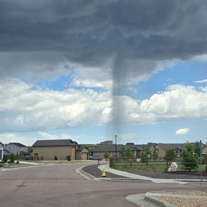 Dark tornado funnel touching down near residential houses under cloudy sky in a wild nature phenomenon.