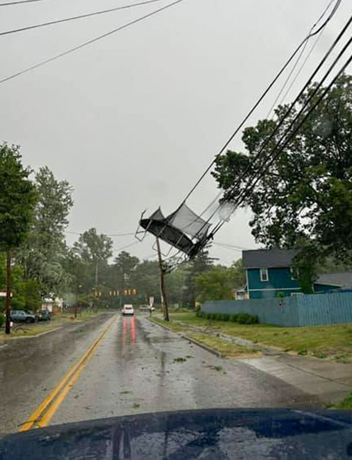 Power lines twisted above a rainy street with a trampoline tangled in the wires, showing nature’s wild impact on urban areas.