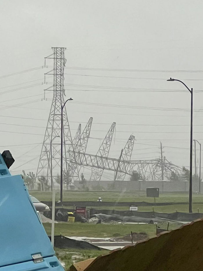 Collapsed electrical towers standing crookedly in a damaged field with overcast sky showing nature’s force on infrastructure.