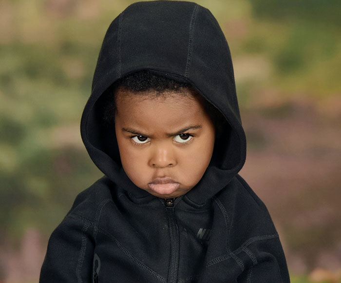 Angry son in first school photo, wearing a black hoodie, with a humorous expression.
