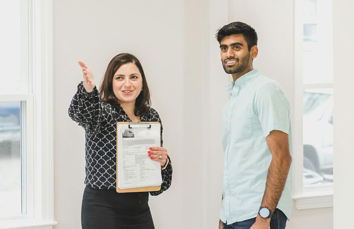 A woman holding a clipboard explaining a point to a man, illustrating jobs that people once respected but realized are done by awful people.