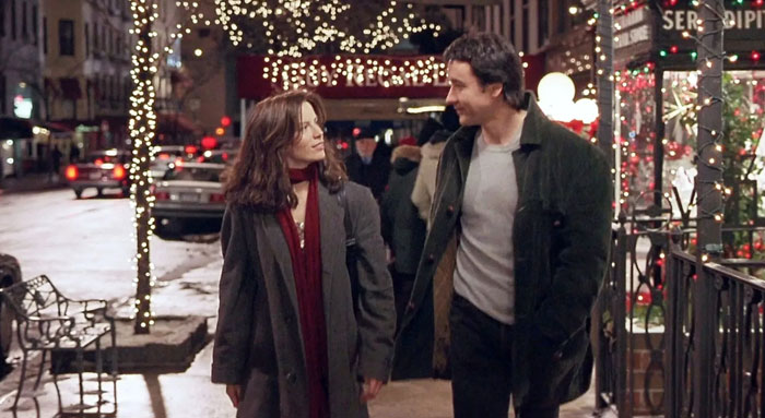 A scene from the movie Serendipity featuring a man and a woman walking side by side on a festive city street at night. Both are dressed in winter coats, with the woman wearing a red scarf, as they exchange smiles and conversation. The street is adorned with holiday lights, and storefronts, including a decorated café, add to the warm, romantic ambiance. In the background, cars and pedestrians contribute to the lively city atmosphere. A scene from the movie Serendipity featuring a man and a woman walking side by side on a festive city street at night. Both are dressed in winter coats, with the woman wearing a red scarf, as they exchange smiles and conversation. The street is adorned with holiday lights, and storefronts, including a decorated café, add to the warm, romantic ambiance. In the background, cars and pedestrians contribute to the lively city atmosphere.