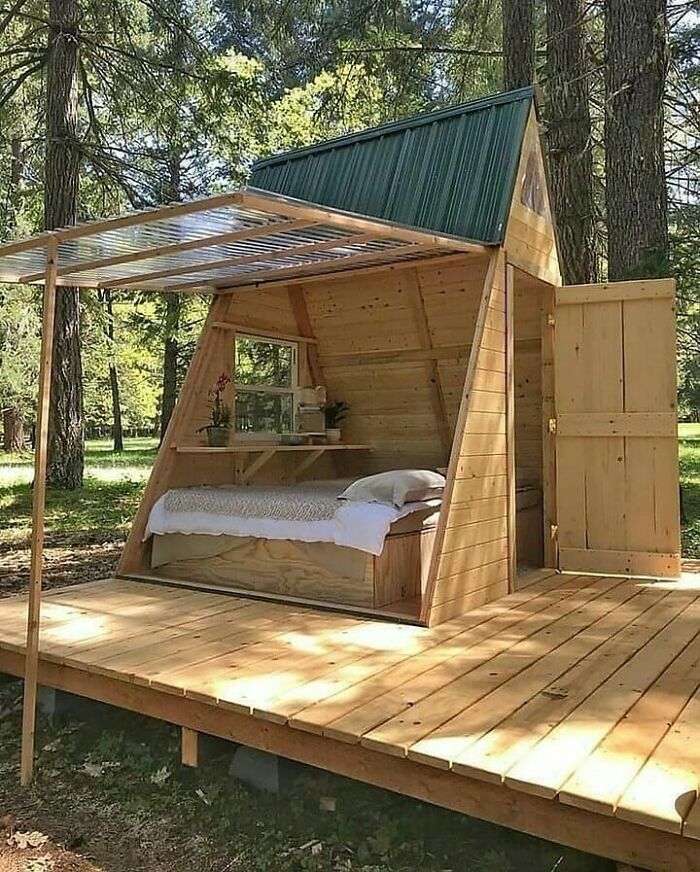 Woodworkers' cool project showcasing a compact wooden cabin with a bed, shelf, and open door in a forest setting.