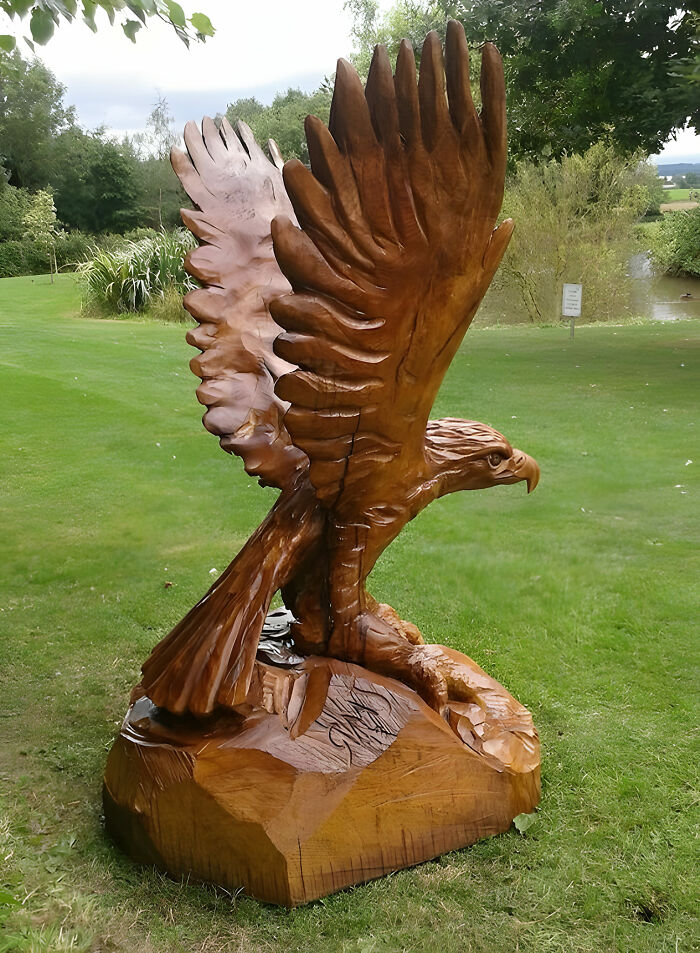 Woodworkers’ impressive eagle sculpture carved from wood, showcasing detailed feathers and perched on a wooden base outdoors.