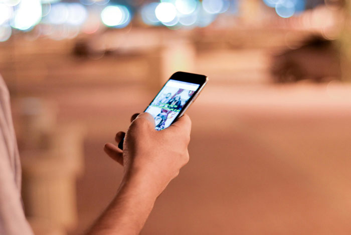 Person holding a smartphone at night, viewing disturbing voicemails received on the device in a blurred outdoor setting.
