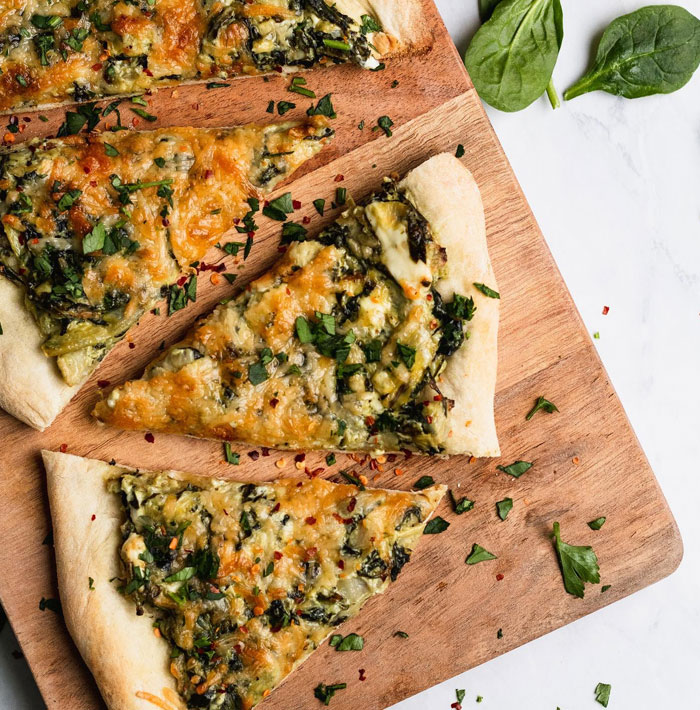 A lunch idea featuring spinach artichoke flatbread slices topped with melted cheese and herbs, arranged on a wooden cutting board. A lunch idea featuring spinach artichoke flatbread slices topped with melted cheese and herbs, arranged on a wooden cutting board.