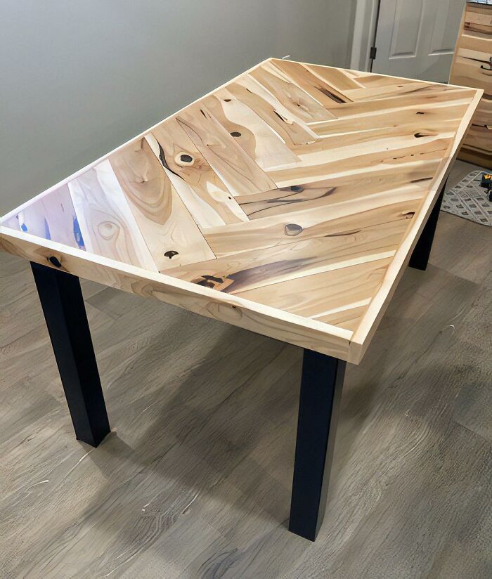 Woodworker’s custom handcrafted wooden table with a geometric patterned top and black metal legs displayed indoors.