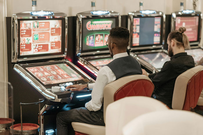 Two men sitting in front of slot machines in a casino, illustrating chilling truths hidden in plain sight.