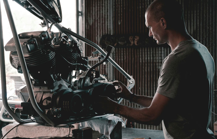 Man working on a motorcycle engine in a dimly lit garage, representing jobs once respected but done by awful people