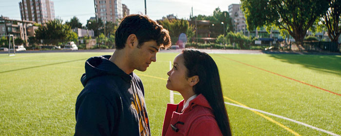 A scene from the movie To All the Boys I've Loved Before featuring a young man and woman standing face-to-face on a bright, sunlit sports field. The man, wearing a hoodie, gazes intently at the woman, who is dressed in a red coat. Both have serious yet affectionate expressions as they share a quiet, intimate moment. The backdrop includes trees, buildings, and the lines of the field, adding to the peaceful, outdoor setting. A scene from the movie To All the Boys I've Loved Before featuring a young man and woman standing face-to-face on a bright, sunlit sports field. The man, wearing a hoodie, gazes intently at the woman, who is dressed in a red coat. Both have serious yet affectionate expressions as they share a quiet, intimate moment. The backdrop includes trees, buildings, and the lines of the field, adding to the peaceful, outdoor setting.