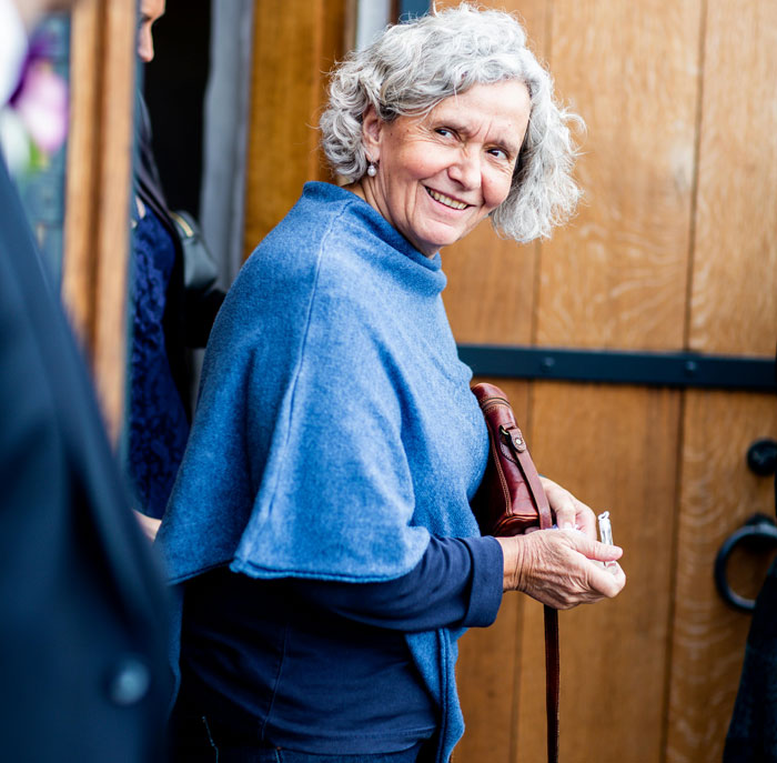 Smiling elderly woman in blue shawl holding a purse, representing chilling truths hidden in plain sight after death.
