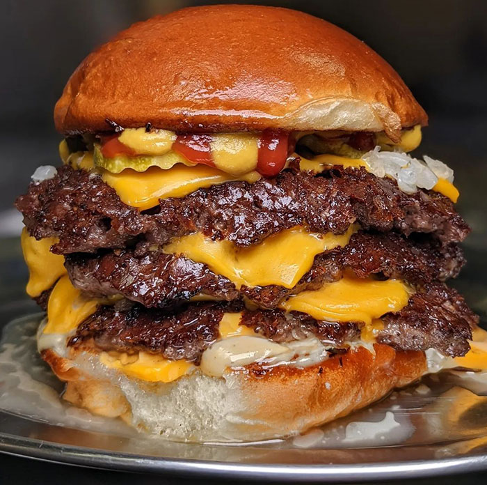 A Lunch idea featuring a stacked smash burger with multiple layers of crispy beef patties, melted cheese, pickles, onions, ketchup, and mustard on a soft bun. A Lunch idea featuring a stacked smash burger with multiple layers of crispy beef patties, melted cheese, pickles, onions, ketchup, and mustard on a soft bun.
