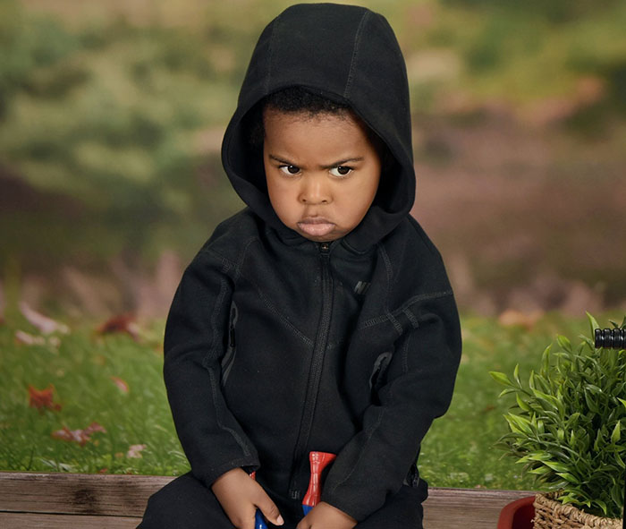 Angry son in first school photo, wearing a black hoodie, with a grumpy expression.