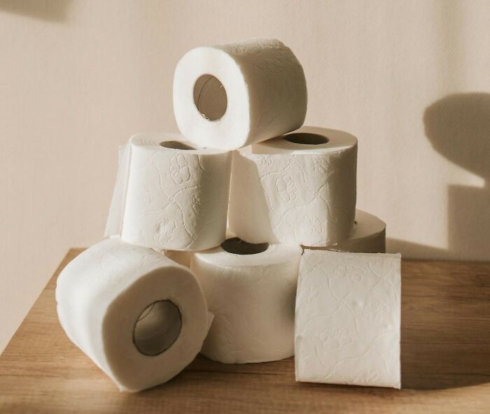 Stack of white toilet paper rolls on wooden surface representing things women want men to finally understand.