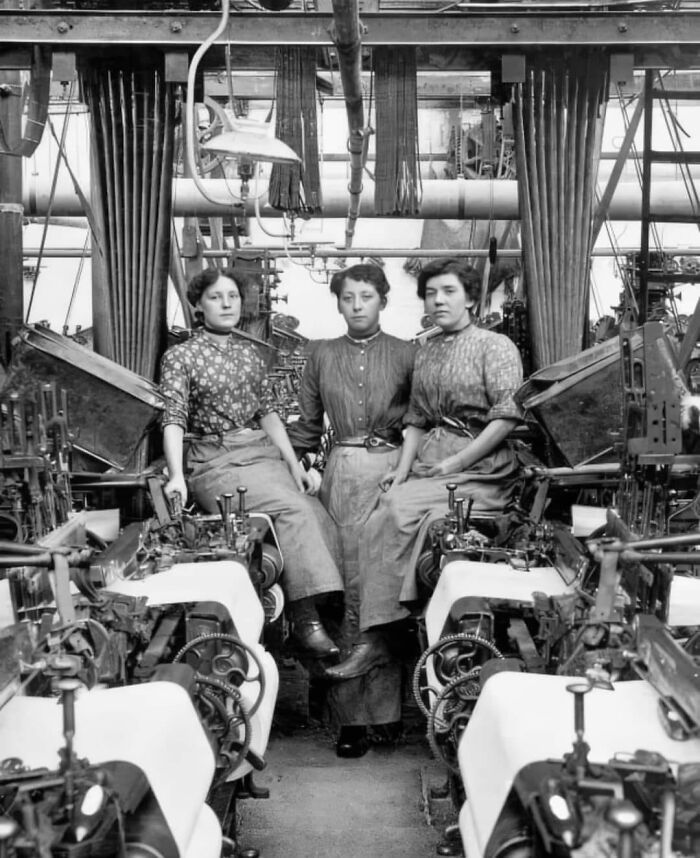 Three women workers posing among vintage industrial machinery in a historical and vintage photos collection.