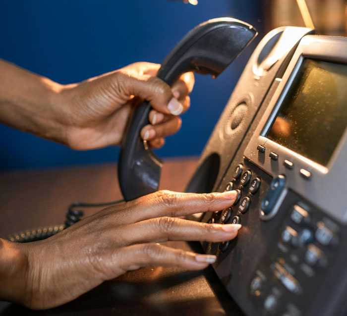 Person holding a phone receiver and pressing buttons on a desk phone, illustrating disturbing voicemails received.