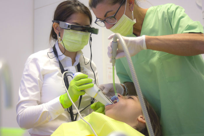Two dental professionals wearing masks and gloves performing a dental procedure on a patient in a clinic