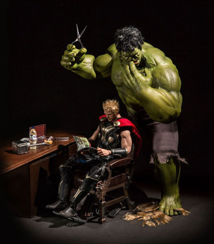 An action figure scene featuring Hulk standing behind Thor, who is sitting in a chair reading a magazine. Hulk is holding a pair of scissors above Thor&rsquo;s head, looking focused as if about to give him a haircut. Thor appears relaxed and unaware of Hulk&rsquo;s actions. 