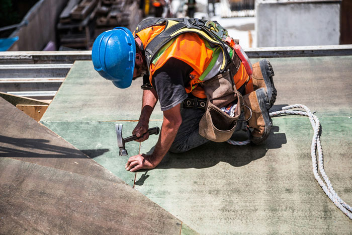 Construction worker in safety gear hammering nails on a roof, illustrating jobs once respected but done by awful people.
