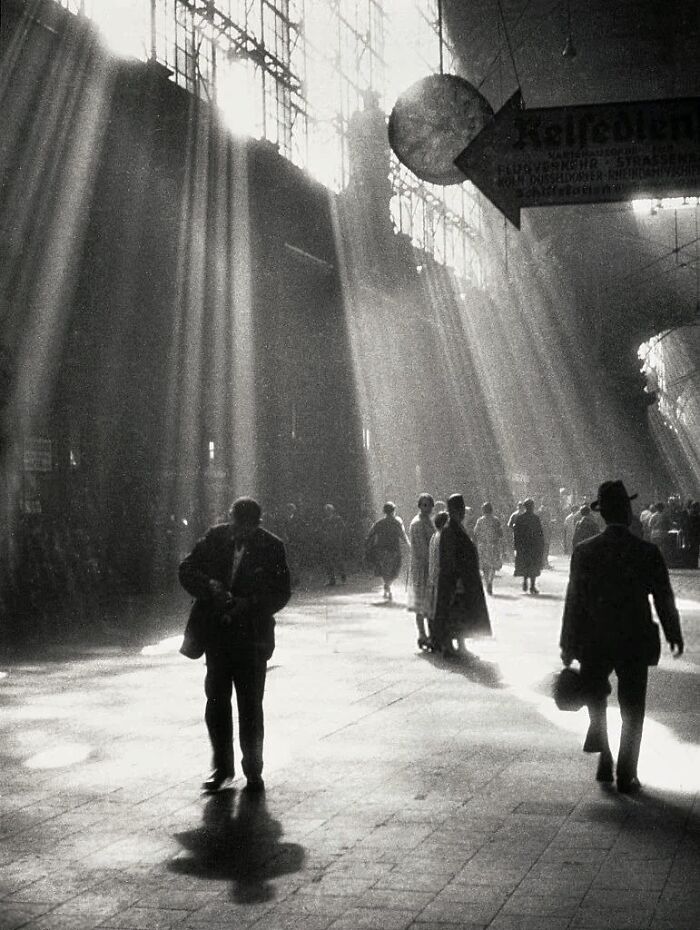 Vintage photo showing people walking in a sunlit indoor space with dramatic light rays and shadows.