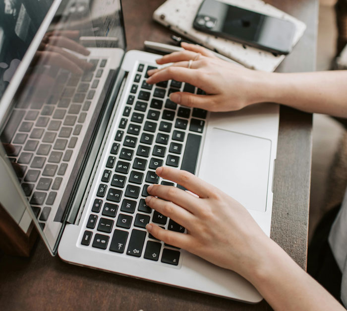 Person typing on a laptop keyboard with a smartphone nearby, illustrating jobs once respected but done by awful people.