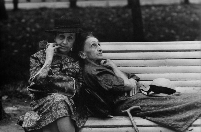 Two elderly women sitting on a bench in a vintage black and white historical photo from a Facebook group sharing vintage photos.