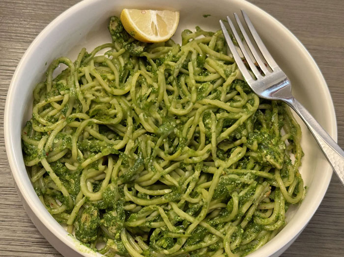A Lunch idea featuring a bowl of spaghetti coated in a green pesto sauce, garnished with a lemon wedge and a fork resting on the side of the bowl. A Lunch idea featuring a bowl of spaghetti coated in a green pesto sauce, garnished with a lemon wedge and a fork resting on the side of the bowl.