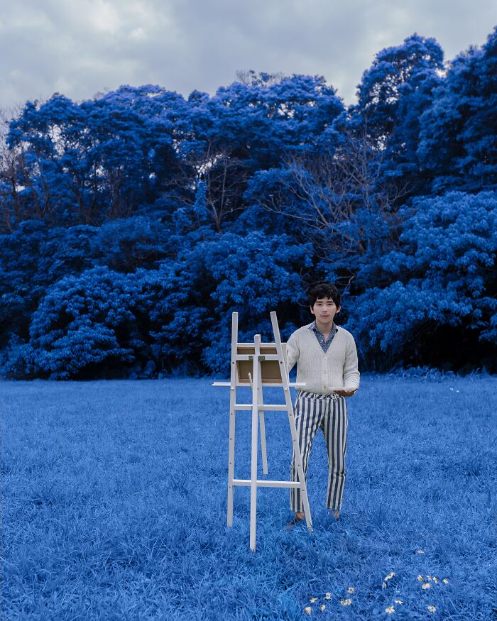 Person standing by an easel in a field with blue trees, showcasing creative advertising photography.
