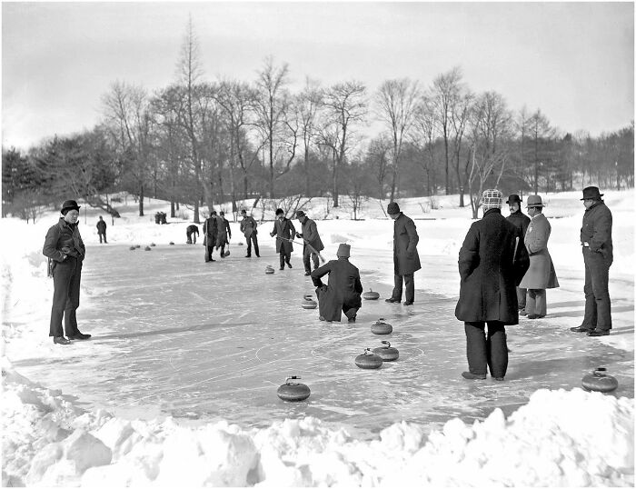 Vintage black and white photo of people playing curling on an outdoor ice rink in a snowy landscape.