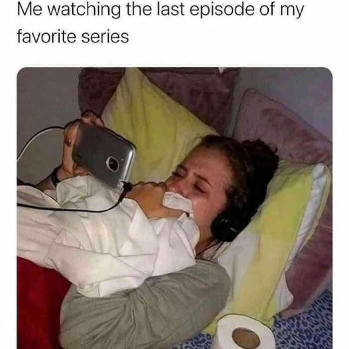 Person in bed watching Netflix on phone, headphones on, visibly emotional with a tissue.