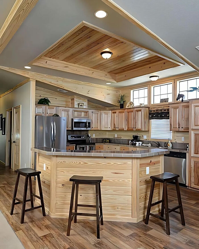Modern kitchen showcasing woodworkers' projects with wooden cabinets, ceiling paneling, and a large kitchen island with stools.
