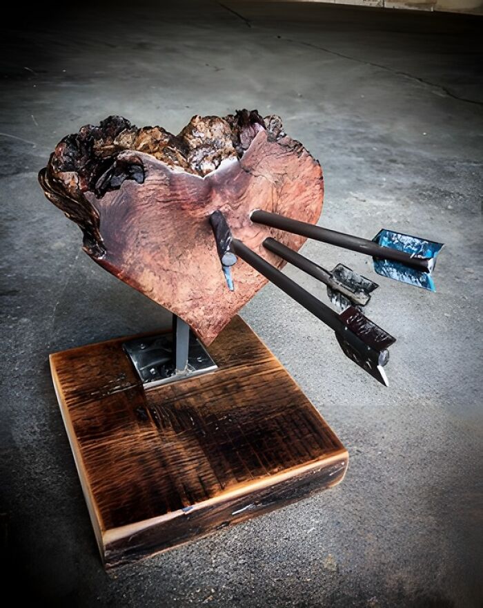 Woodworking project featuring a heart-shaped wooden sculpture pierced by metal arrows on a wooden base.