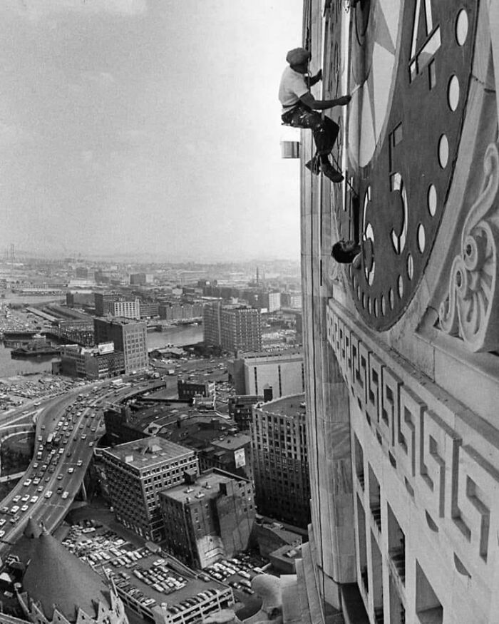 Two workers high above a city painting a giant clock face in a historical and vintage photo.
