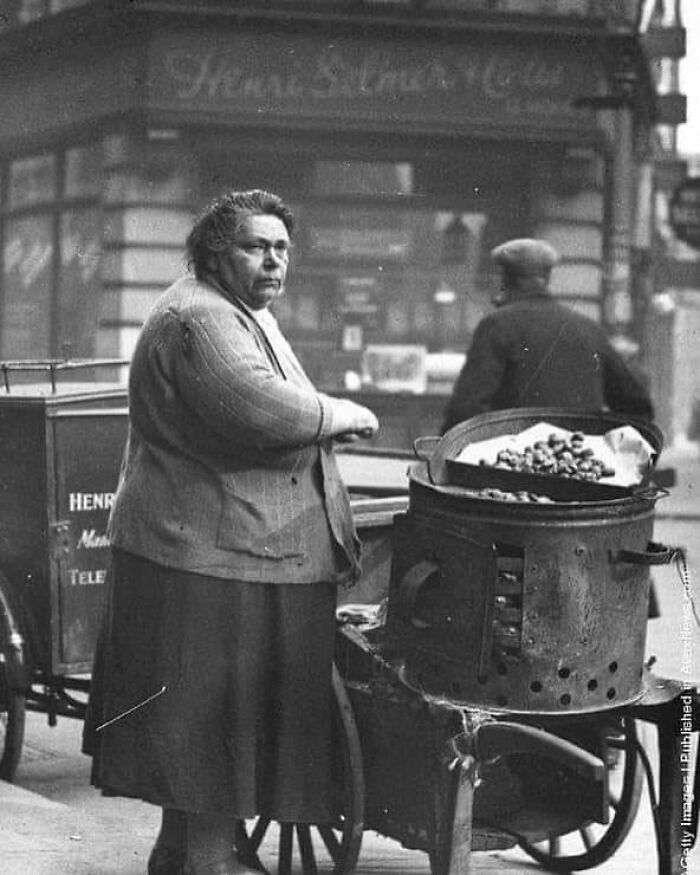 Woman roasting chestnuts on street with vintage cart in historical black and white photo from a vintage photos collection.