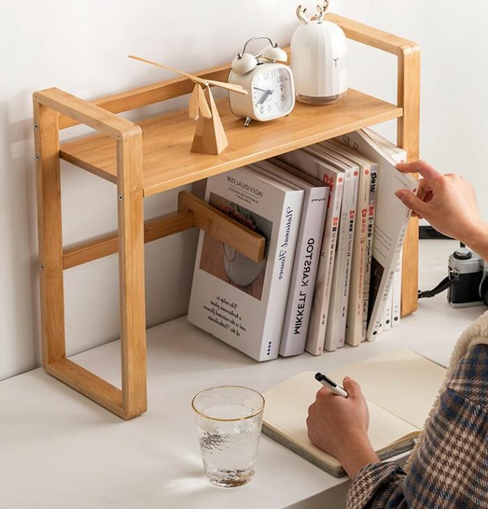 Woodworkers’ cool wooden desk shelf holding books and decor, with a person writing in a notebook nearby.