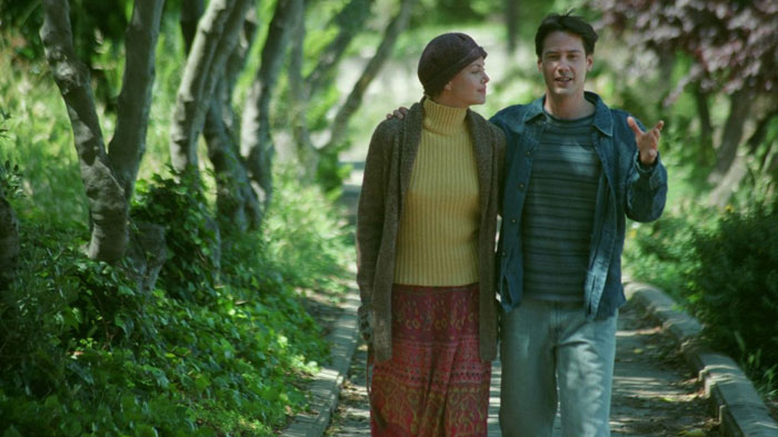 A scene from the movie Sweet November featuring a man and a woman walking arm-in-arm down a tree-lined path. The woman, wearing a headscarf, a yellow turtleneck, and a patterned skirt, looks affectionately at the man. The man, dressed casually in a jacket and jeans, gestures while talking, smiling as they walk together in a peaceful, green setting. A scene from the movie Sweet November featuring a man and a woman walking arm-in-arm down a tree-lined path. The woman, wearing a headscarf, a yellow turtleneck, and a patterned skirt, looks affectionately at the man. The man, dressed casually in a jacket and jeans, gestures while talking, smiling as they walk together in a peaceful, green setting.
