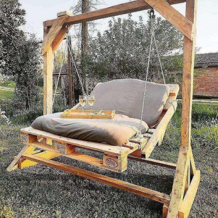 Woodworker crafted a wooden pallet swing with cushions hanging from a sturdy frame, perfect for outdoor relaxation.