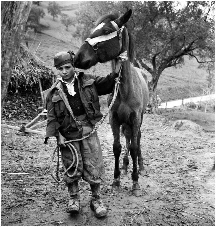 Young boy in vintage clothing holding a horse in a muddy outdoor setting, showcasing historical and vintage photos.