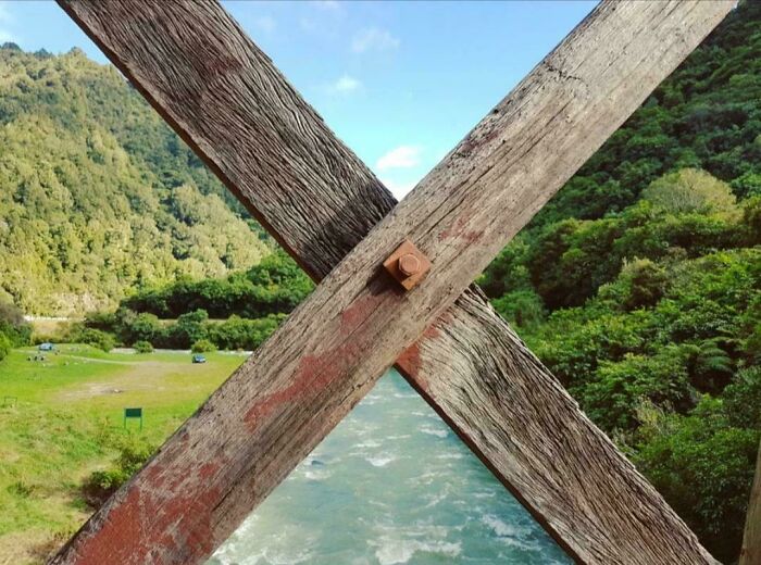 Wooden beams crossing over a vibrant green landscape and river, showcasing nature's beauty.